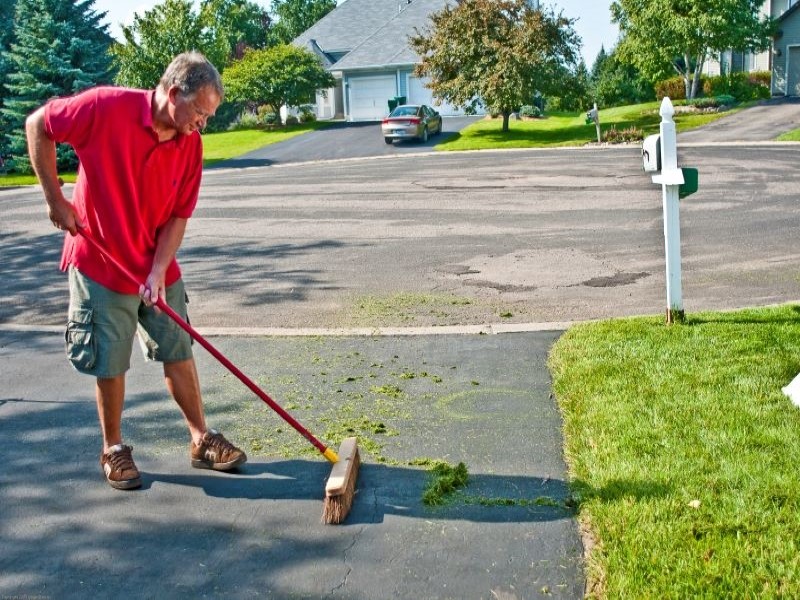 Man sweeping Grass clippings off driveway and into lawn
