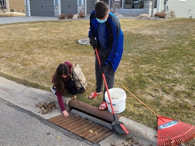Two teens with a broom cleaning out a stormdrain