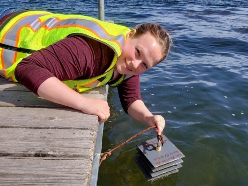 woman on lake dock checking zebra mussel plates