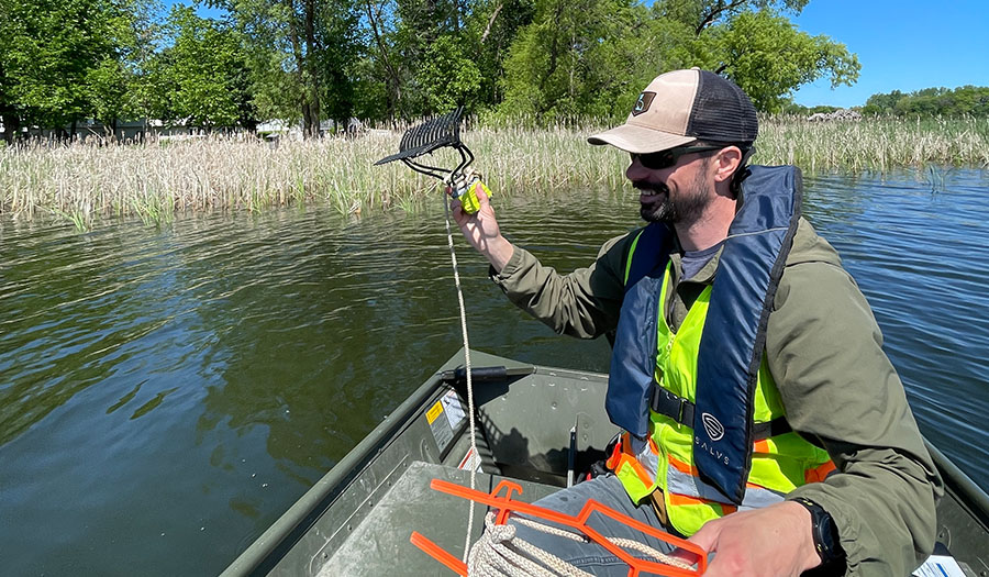 Watershed staff member sitting in a boat, preparing to throw a vegetation rake into the water.